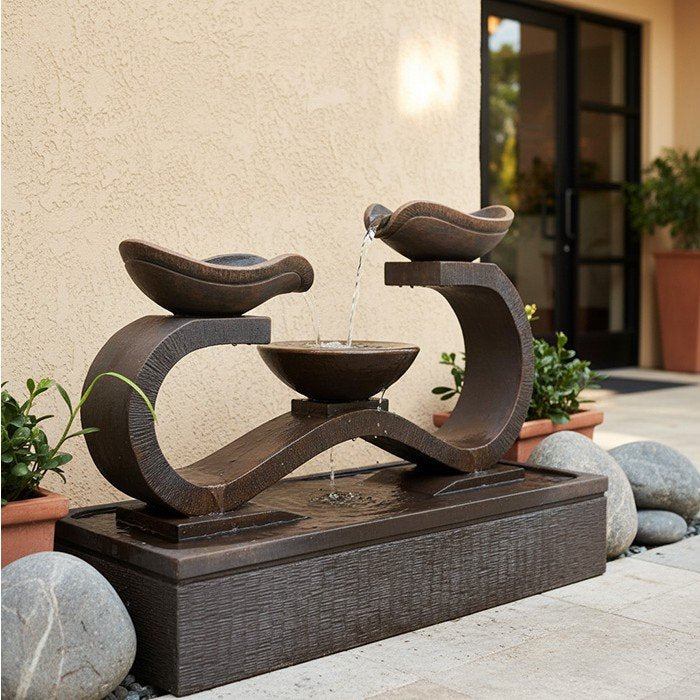 Exaco Infinity fountain in Rust on a patio beside a stucco wall and potted plants.