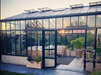 Modern Exaco Janssens Gigant Greenhouse with brick base, glass walls, and open door at sunset