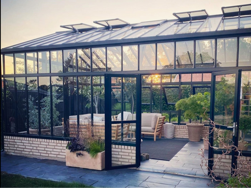 Modern Exaco Janssens Gigant Greenhouse with brick base, glass walls, and open door at sunset
