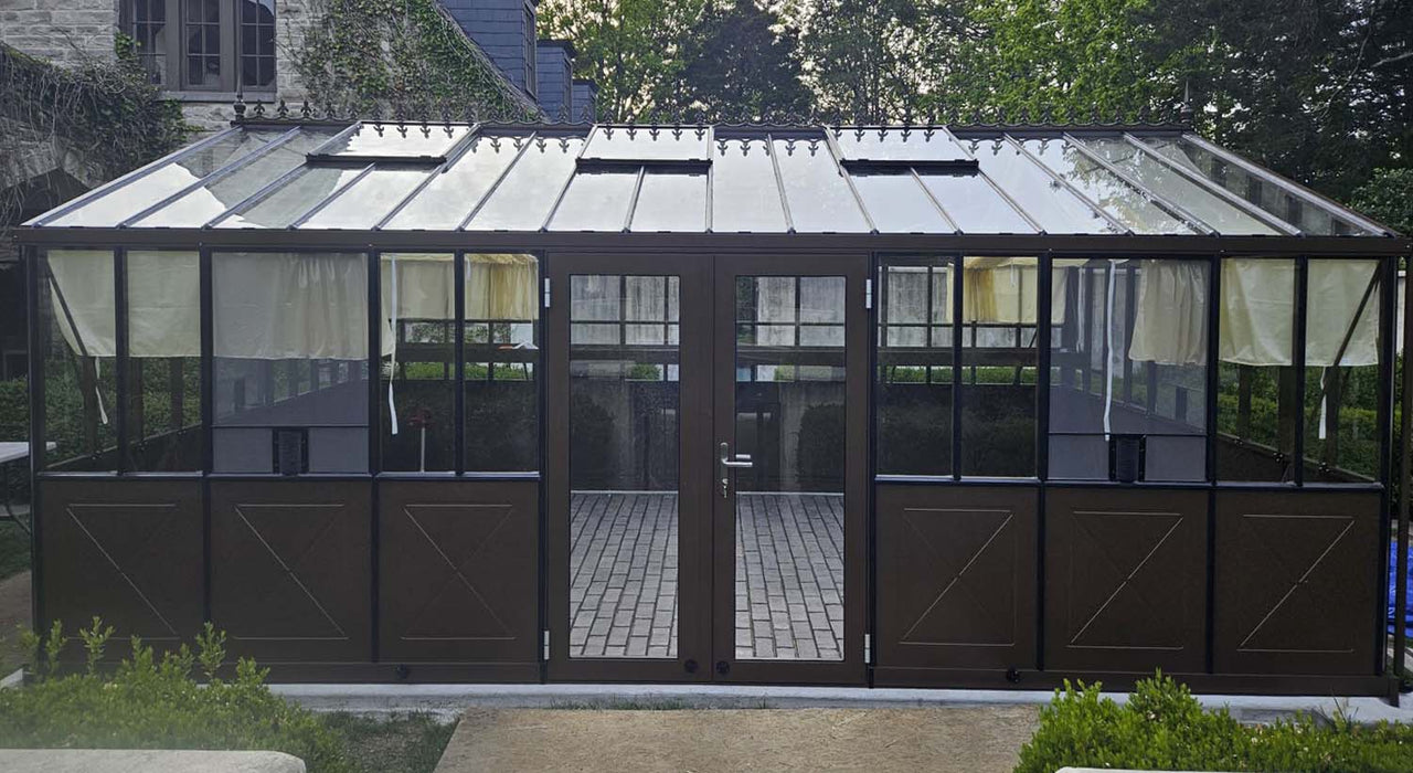 Front view of Exaco Janssens Retro Royal Victorian VI Greenhouse in terra brown, showcasing X-pattern lower panels, double doors, and clear roof panels.