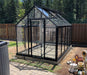 Exaco Janssens Royal Victorian VI 23 greenhouse with black aluminum frame and clear tempered glass panels, set on a foundation in a fenced backyard.