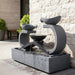 Infinity fountain by Exaco in Slate finish, angled in a lush garden setting surrounded by flowering plants.