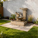Exaco Trio Bowl outdoor water fountain with cascading tiers set on a modern patio against a privacy wall and landscaped garden