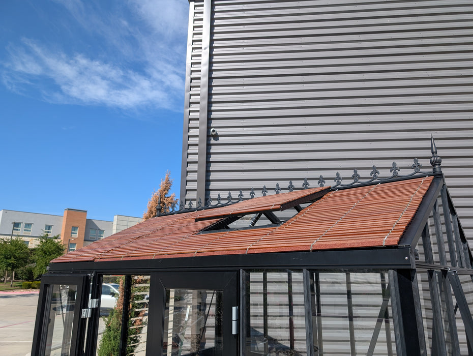 Royal Victorian 23 greenhouse fitted with wood slatted shades by Exaco, shown in an outdoor display with open roof vents for cooling and natural light control.