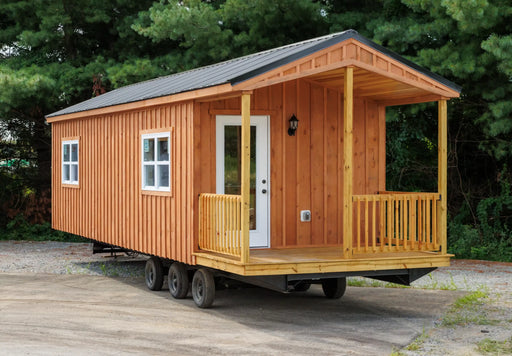 Front exterior view of the Oasis Tiny Estates Firestack Cabin featuring a welcoming porch and natural wooden siding, set against a lush green background.