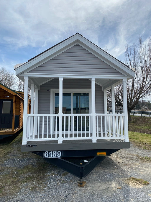 Exterior front view of the Champion Home with Loft by Oasis Tiny Estates, featuring a porch and white railing.