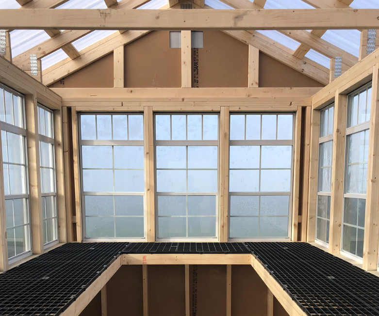 Interior view of an Ez-Fit Kits Greenhouse Shed Kit showing wood framing, roof trusses, and polycarbonate window panels with bench framing installed