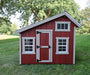 Front view of EZ-Fit Playhouse Kit in red with white trim, double windows and barn-style door, outdoor wooden shed on green lawn