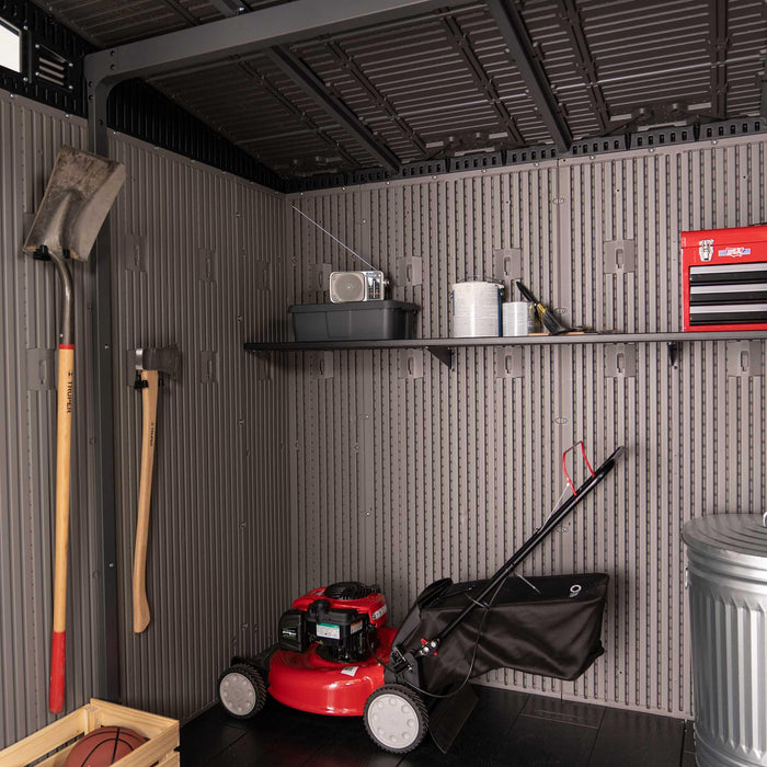 Full interior view of the Lifetime 60542 storage shed with wall-mounted shovels, built-in shelving holding containers and a toolbox, red lawn mower, and trash can