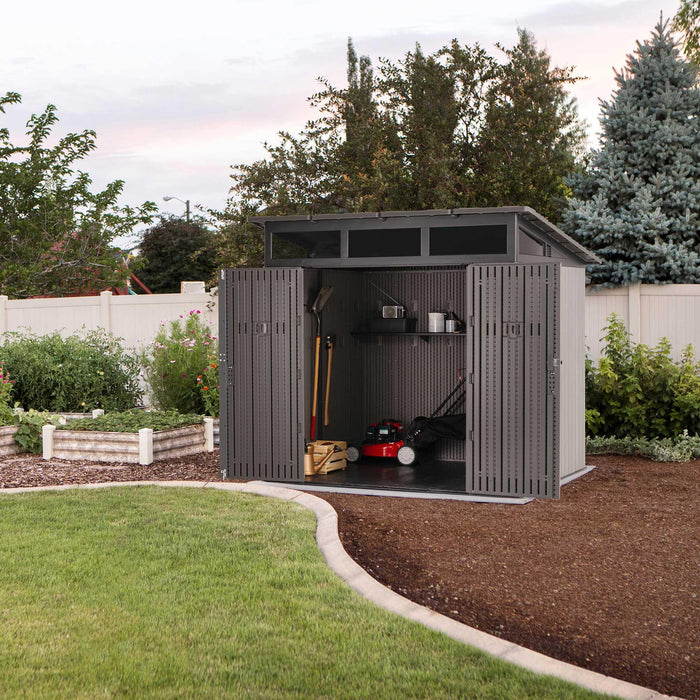 Lifetime 60542 Farmhouse Storage Shed with open double doors in a backyard garden at dusk, showing interior with lawn mower, garden tools, and built-in shelving