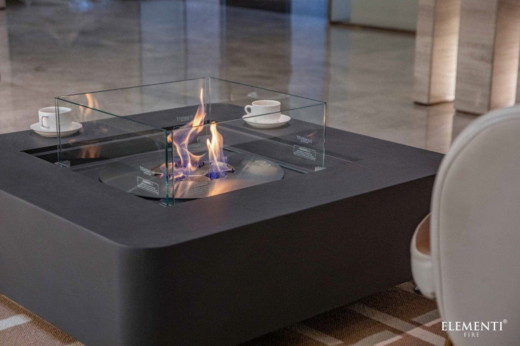 Elementi Perth Fire Table in slate black with blue-orange flames lit and clear glass guard