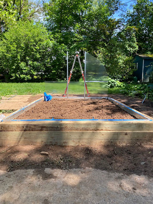 Wooden foundation base prepared for the Exaco Hoklartherm Riga 4 Greenhouse, showing level soil bed and ladder setup in a backyard garden.