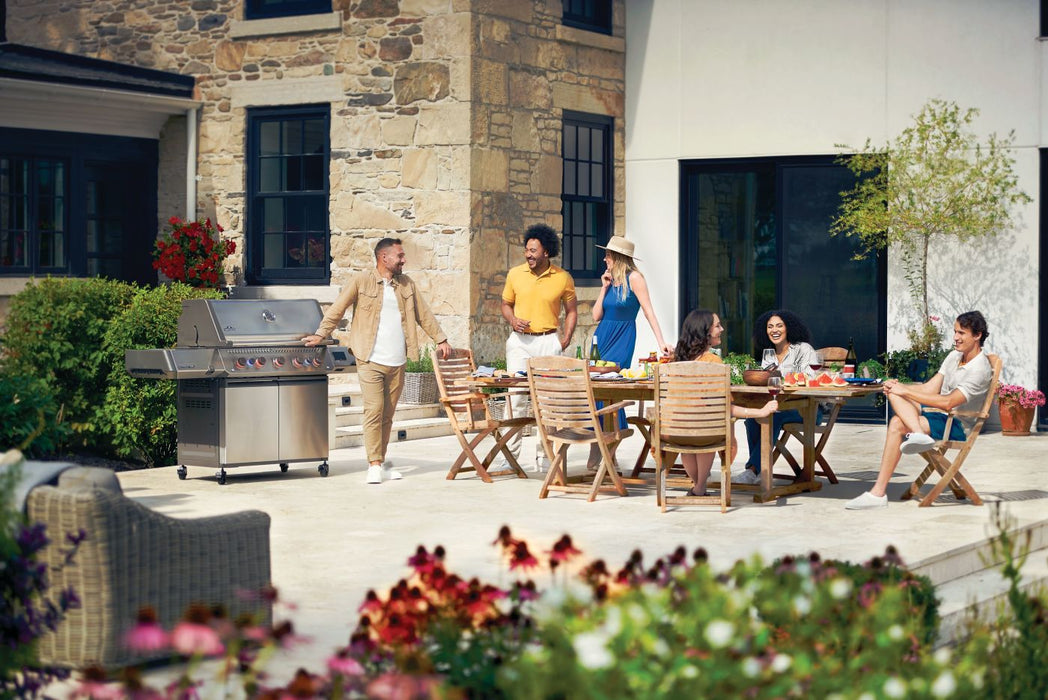 Group of friends enjoying a meal outdoors next to Napoleon Grills Prestige® 665 RSIB grill on a stone patio