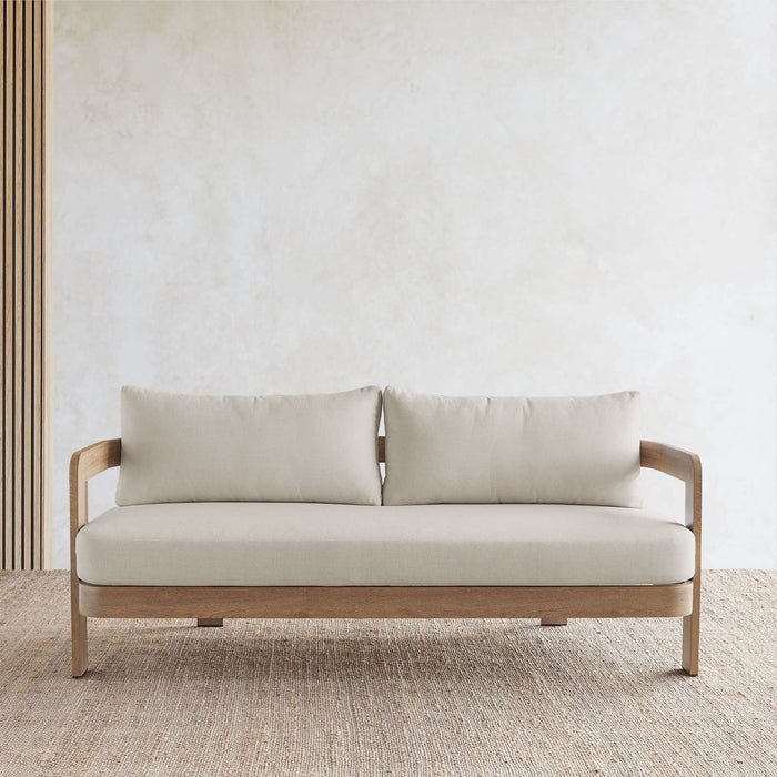 Front angle view of the Real Flame Arlo Outdoor Seat Sofa with Cushions placed on a textured rug and minimalist background, showcasing armrest details.