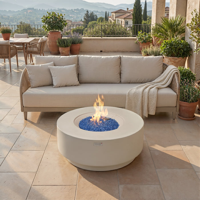 Round concrete fire pit table in frosted cream white with blue glass and open flame on an outdoor patio near a beige sofa