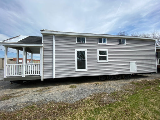 Full-length side view of the Champion Home with Loft by Oasis Tiny Estates, featuring a porch with a white railing and windows.