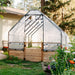 Front view of the 8x12 Greenhouse Garden in a Box, cedar gate and mesh panels below a clear canopy with roll-up windows in a flowering yard