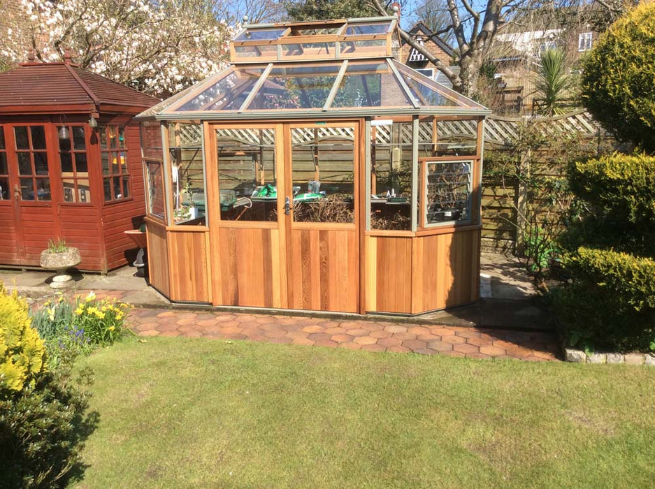 The Alton Cedar Structure Evolution Octagonal 9x11, placed in a vibrant garden with a rustic outdoor setting.