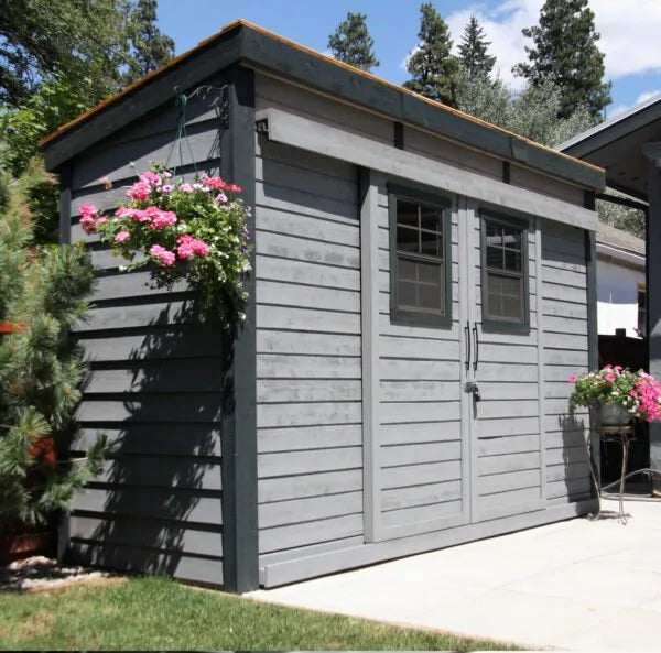 GardenSaver 12x4 cedar shed painted gray with black trim and sliding doors installed on modern backyard patio.
