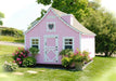 Charming outdoor view of the Little Cottage Company Gingerbread Cottage Playhouse adorned with pink siding and heart-shaped window.