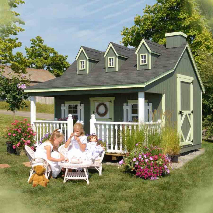 Two girls enjoying a tea party in a sunny outdoor setting, with the Pennfield Cottage Playhouse in the background.