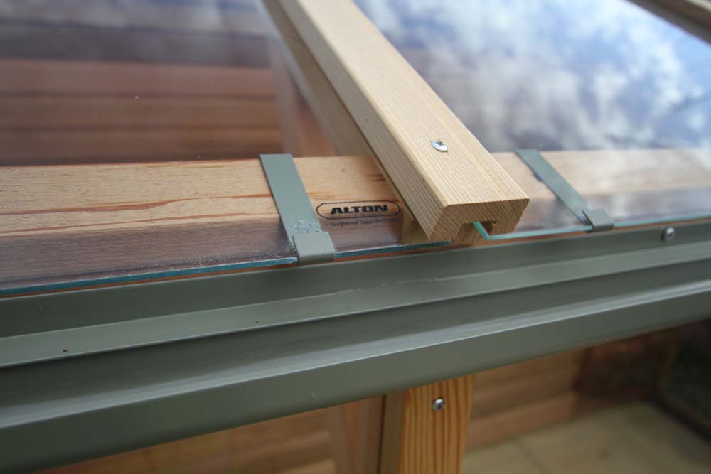 Close-up of the glass panel and wooden roof structure of the Alton Cedar Fusion Greenhouse with the brand logo visible.