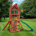 Rear view of the Nantucket II cedar swing set in a lush backyard featuring treehouse roof, green slide, rock wall, sandbox, and tic-tac-toe panel