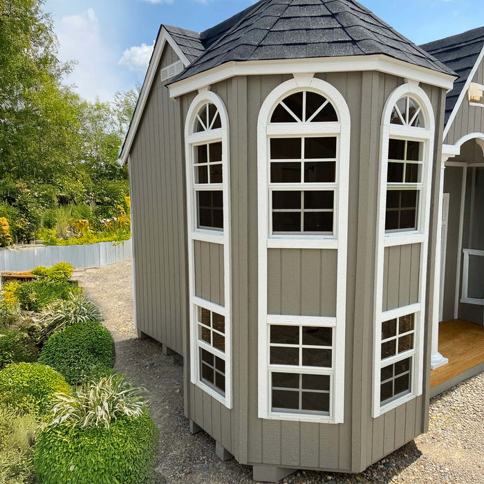 Exterior of Little Cottage Co. Grand Portico Mansion featuring tall bay windows with white trim against gray siding, elegant playhouse design
