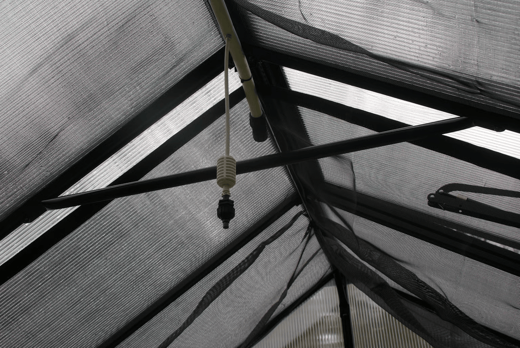 End nozzle of Riverstone Internal Watering System installed inside greenhouse roof frame for plant misting.