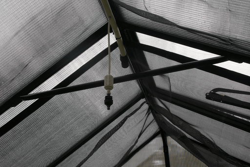 End nozzle of Riverstone Internal Watering System installed inside greenhouse roof frame for plant misting.