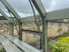 An external view of the Alton Cedar Structure Durham Greenhouse, displaying its sturdy cedar construction in a natural garden setting.