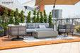 An Elementi Milano Collection patio furniture arrangement on a wooden surface, including a light grey sofa with dark and light patterned cushions, two grey rope armchairs with light cushions