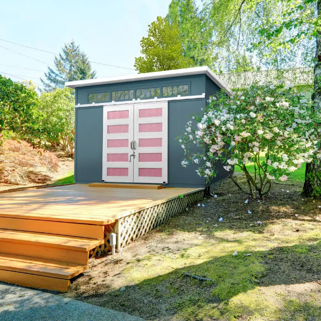 Handy Home Palisade backyard shed with modern design, featuring light pink double doors, a spacious deck, and a gray exterior. 