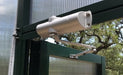 The Exaco Hinged Door Accessories, a silver automatic door closer by Exaco, is mounted on a green metal door frame with clear panels and trees visible in the background.