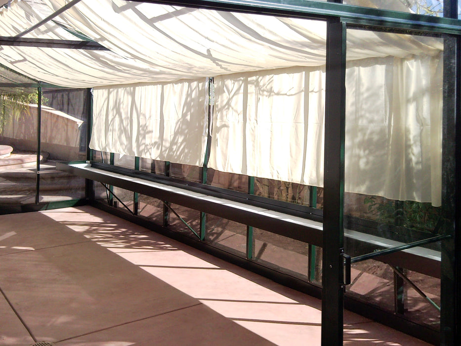 Interior of Royal Victorian VI 46 greenhouse by Exaco Janssens featuring ceiling curtains for shade, a long plant shelf, and ample growing space.