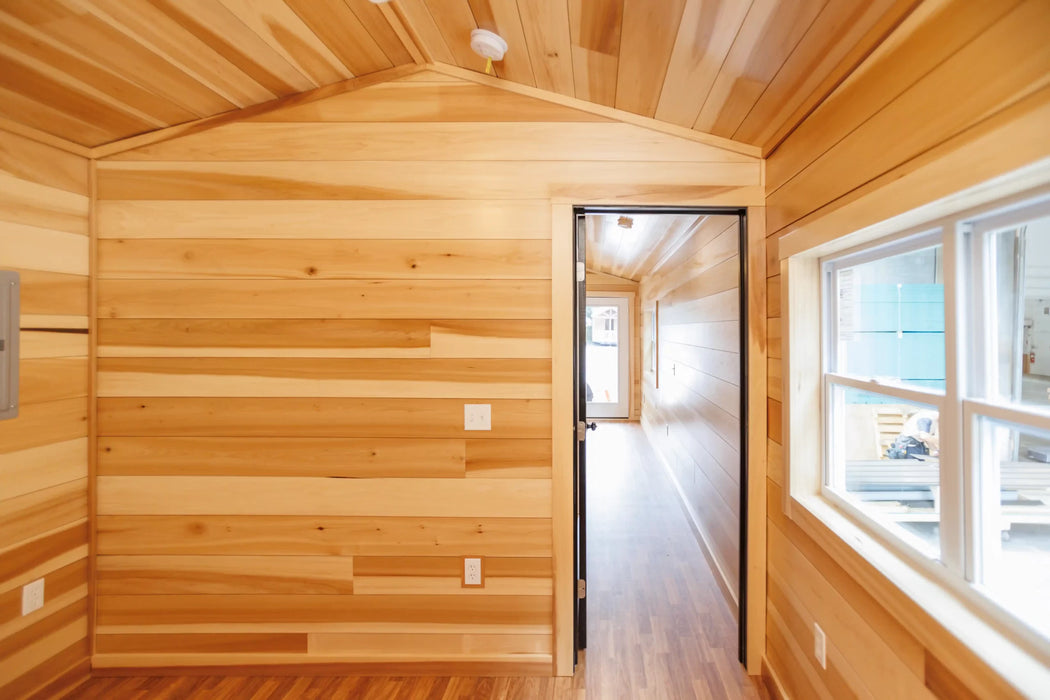 Long interior hallway of the Oasis Tiny Estates Firestack Cabin showing a wooden paneled hallway leading to brightly lit rooms, emphasizing spacious design in a compact space.