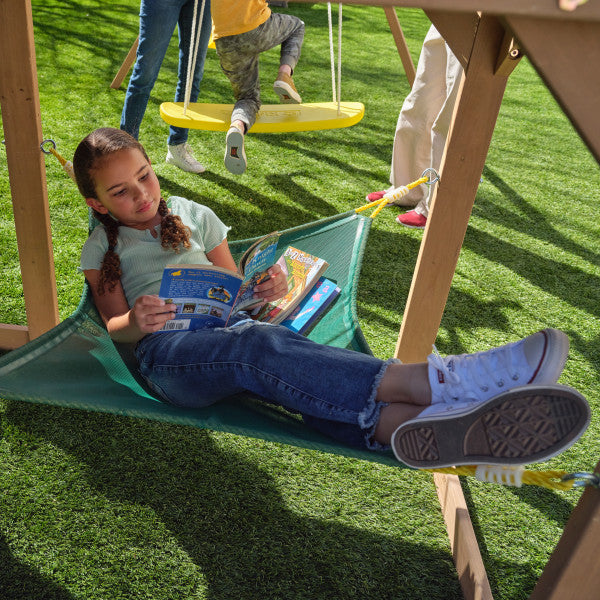 Kid in a hammock reading a book on the outdoor wooden playset