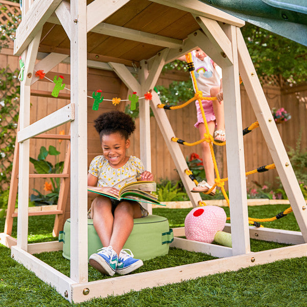 Kid reading a book under the wooden emerald playset