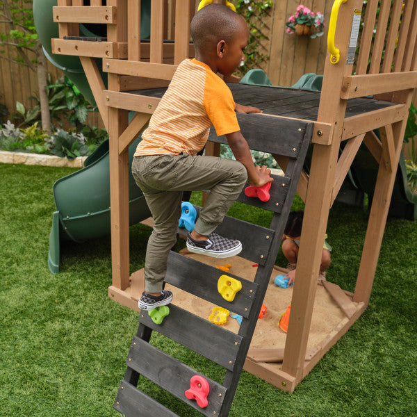 Kid climbing up the rock wall of the wooden timberlake swing set