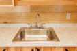 Close-up of the kitchen area in the Oasis Tiny Estates Firestack Cabin, featuring a stainless steel sink set against a marble countertop and wooden cabinetry.