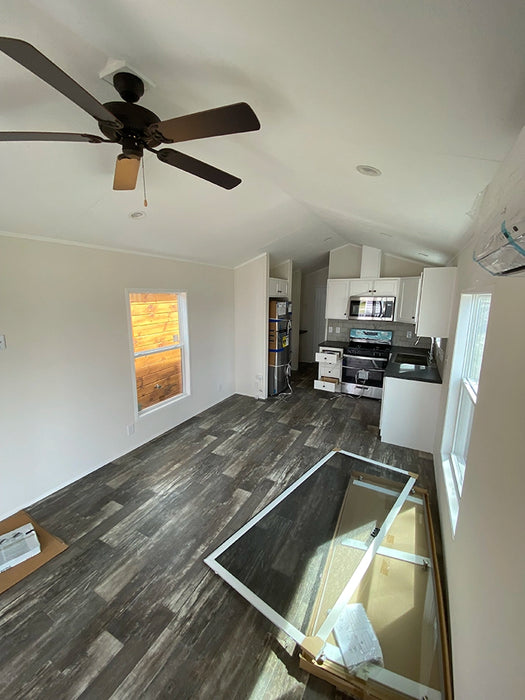 Wide-angle shot of the kitchen area inside the Champion Home No Loft, displaying the living room, kitchen, and a ceiling fan.