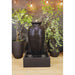 Large decorative amphora floor fountain with square reservoir and glossy finish styled between tall indoor plants.