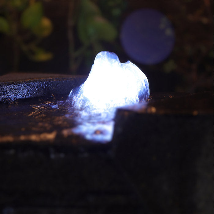 Close up of Yang water fountain LED light at the top, highlighting glowing water feature and textured stone surface at night.