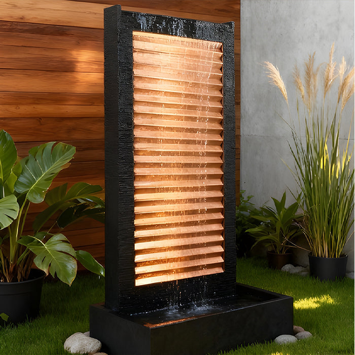 LED lighted modern wall fountain with glowing copper panel and black frame, installed in landscaped patio setting.