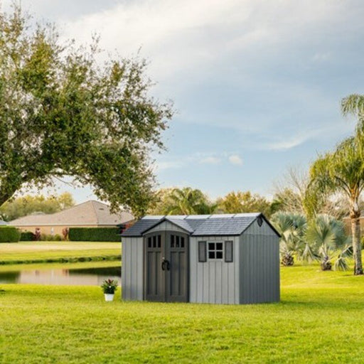 Lifetime 12.5x8 ft. side entry storage shed installed by a lake with palm trees, front angle, closed doors.