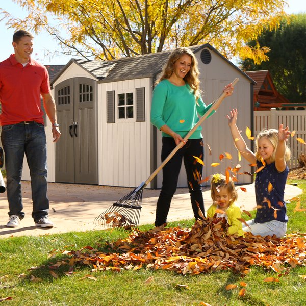Family raking autumn leaves in front of the Lifetime 15x8 ft. storage shed, closed double doors.