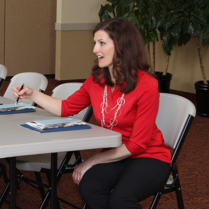 Woman seated on Lifetime 4-Pack Classic Folding Chair in putty during conference setup with folding tables