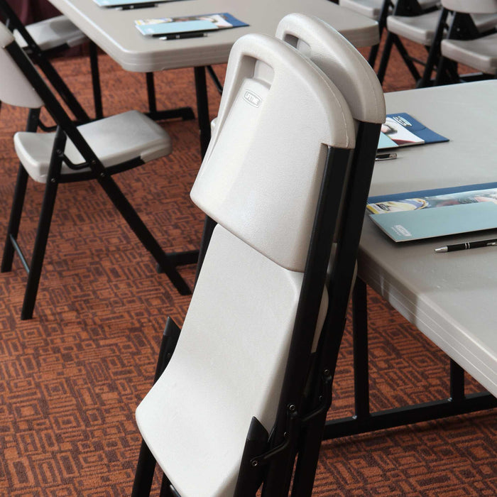 Folded Lifetime 4-Pack Classic Folding Chair in putty leaning against table with black steel frame in meeting room