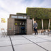 Man opening the double doors of a Lifetime Farmhouse Shed 60542 on a modern concrete patio, interior stocked with sports gear, grill, ladder, and shelved items