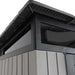Close-up of the Lifetime Farmhouse Shed 60542 roofline corner showing dark overhang, shatter-resistant skylight window frame, and wood-grain wall panels